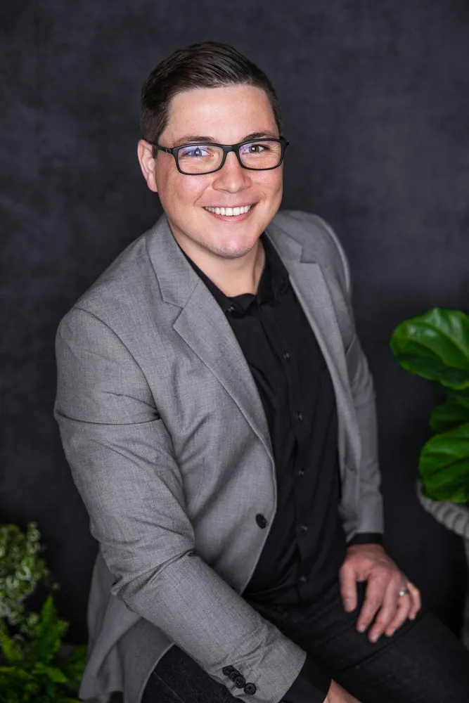 Caleb in a gray blazer, seated beside a fiddle-leaf fig