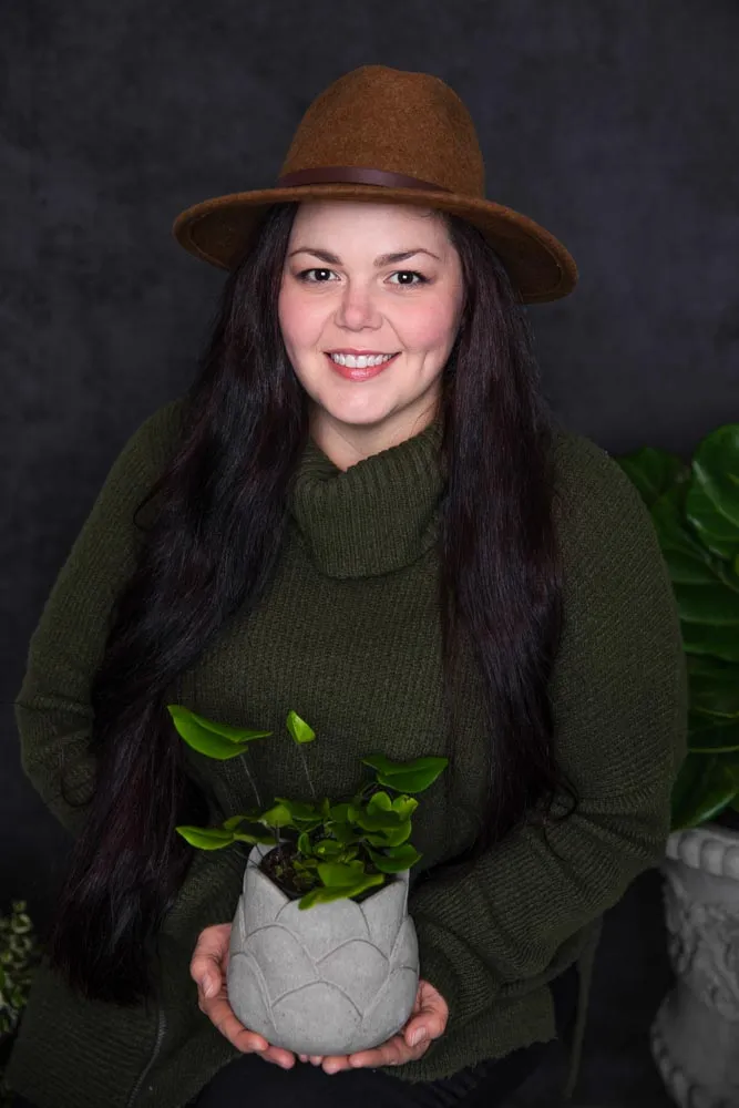 Tiffany in a brown felt hat, holding a small potted peperomia in a scalloped concrete pot