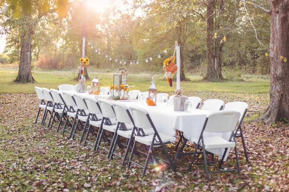Long harvest table set outdoors for an autumn evening, with sunflowers, dried grasses, lanterns and jar candles down its length