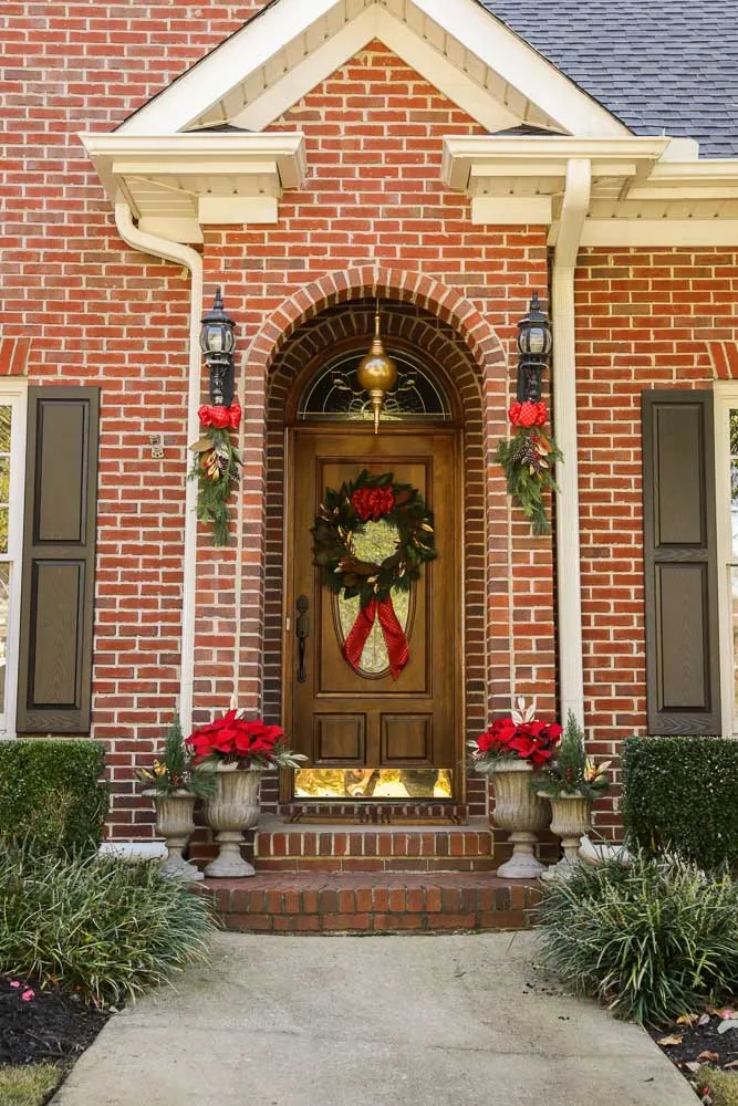 Arched brick entry fully dressed for the holidays: matched stone urns planted with cypress and magnolia, garland on the carriage lights