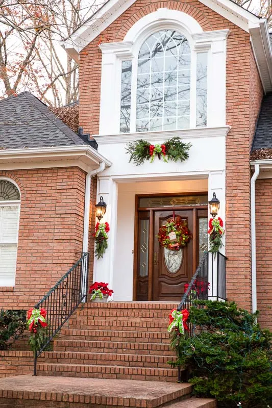 Two-story brick entry dressed for the holidays: garland over the portico, a wreath centered on the arched window, poinsettia down the stair rail
